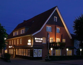 Außenansicht Backsteingebäude mit spitzem Giebeldach, beleuchteten Fenstern und Hotel-Restaurant-Schriftzug bei Nacht.