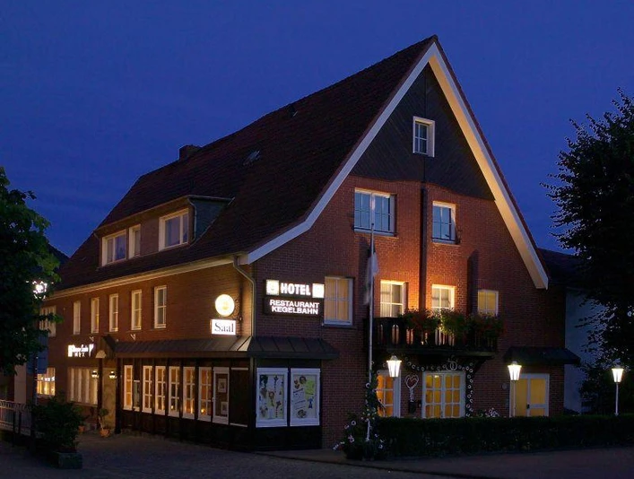 Außenansicht Backsteingebäude mit spitzem Giebeldach, beleuchteten Fenstern und Hotel-Restaurant-Schriftzug bei Nacht.