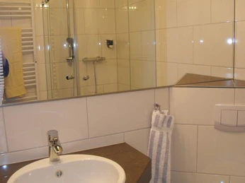 Badezimmer Ein modernes Badezimmer mit weiß gefliesten Wänden, Waschbecken, Dusche und Handtuchhalter.