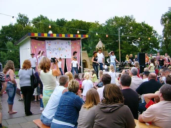 Ferienanlage Regenbogen: Kinderanimation Kinderanimation mit Tanzaufführung auf der Bühne einer Ferienanlage, umgeben von gespanntem Publikum.