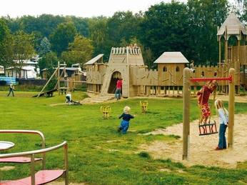Kinder spielen auf einem weitläufigen Abenteuerspielplatz aus Holz mit Rutsche und Schaukeln.