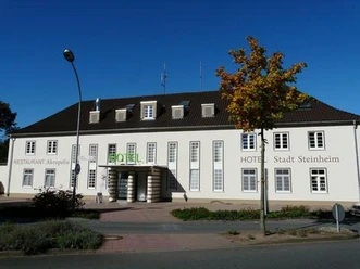 Ein weißes Gebäude mit braunem Dach, vertieften Eingängen, und dem Namen "Hotel Stadt Steinheim".