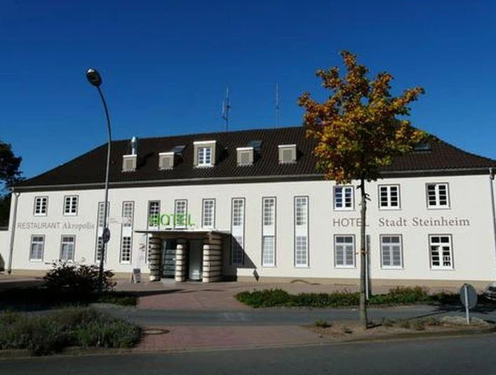 Ein weißes Gebäude mit braunem Dach, vertieften Eingängen, und dem Namen "Hotel Stadt Steinheim".