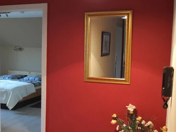 Vita-Farm Bergmann-Scholvien: Schlafzimmer Ein Schlafzimmer mit einem Doppelbett und Holzmöbeln, angrenzend ein Flur mit roter Wand und Spiegel.