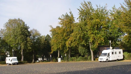 Wohnmobilstellplatz am Werl Rheda-Wiedenbrück Zwei Wohnmobile stehen auf einem von Bäumen umgebenen Parkplatz; Herbstlaub bedeckt den Boden.