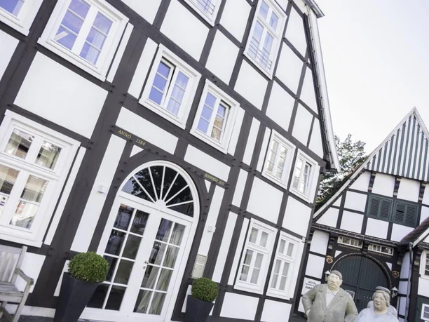 Fachwerkgebäude mit modernem Eingang und Bronzeskulpturen vor einem strahlend blauen Himmel.