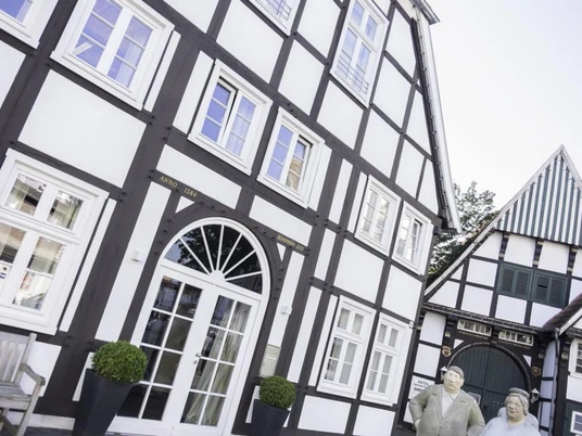 Altstadt mit Alltagsmenschen Rheda-Wiedenbrück Fachwerkgebäude mit modernem Eingang und Bronzeskulpturen vor einem strahlend blauen Himmel.