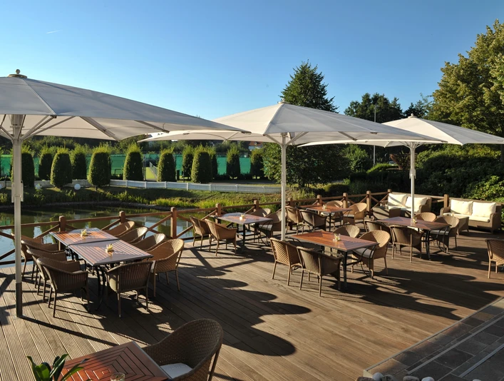 Seeterrasse Restaurantterrasse mit Holzboden, Tischen und Stühlen im Freien, umgeben von grüner Natur.