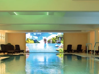 Wellnessbereich im Court Hotel Wellnessbereich mit großem Pool, dekoriert mit Wandbildern tropischer Landschaften und Liegestühlen.