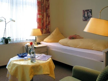 Ein Einzelzimmer mit einem bequemen Bett, einem Tisch mit Getränkeauswahl und warmem Licht.