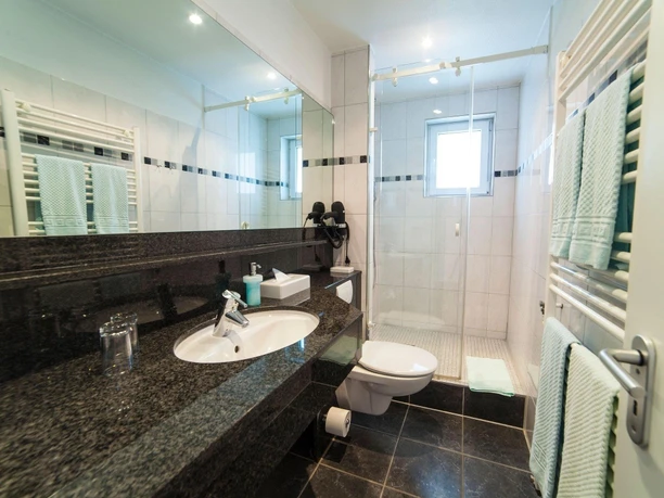 Modernes Badezimmer mit dunklem Granitwaschtisch, bodentiefer Dusche und hell gefliesten Wänden.