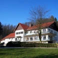 Naturfreundehaus Teutoburg Großes, modernes Gebäude mit rotem Dach, umgeben von Wald und Wiese an einem sonnigen Tag.