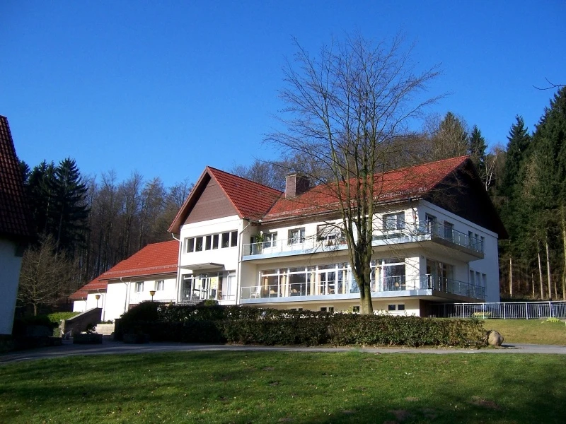 Naturfreundehaus Teutoburg Großes, modernes Gebäude mit rotem Dach, umgeben von Wald und Wiese an einem sonnigen Tag.