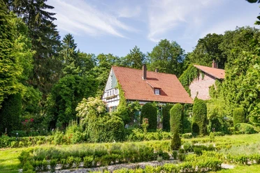 Panoramablick auf das Alte Forstamt im Teutoburger Wald Traditionelles Gebäude aus Fachwerk mit rotem Dach, umgeben von grüner Natur und Bäumen im Sommer.