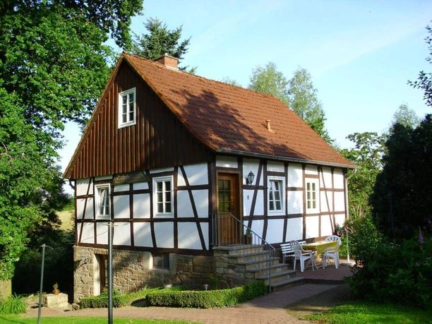 Urlaub auf dem Bauernhof: Willkommen auf dem Lüdekingshof! Fachwerkhaus mit grüner Umgebung, rotem Ziegeldach und Gartenmöbeln auf einer Terrasse vor dem Haus.