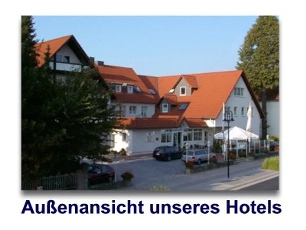 Hotel mit roten Dächern und weißen Fassaden, umgeben von Bäumen, Vorderansicht mit Eingang.