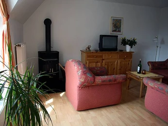 FeWo-Wohnzimmer Einladendes Wohnzimmer mit roten Sofas, einem Holzofen, Fernseher und hellem Holzboden.