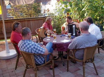 Aussengastronomie Gruppe von Männern sitzt bei Getränken draußen, mit Gitarre und Akkordeon für Musikunterhaltung.