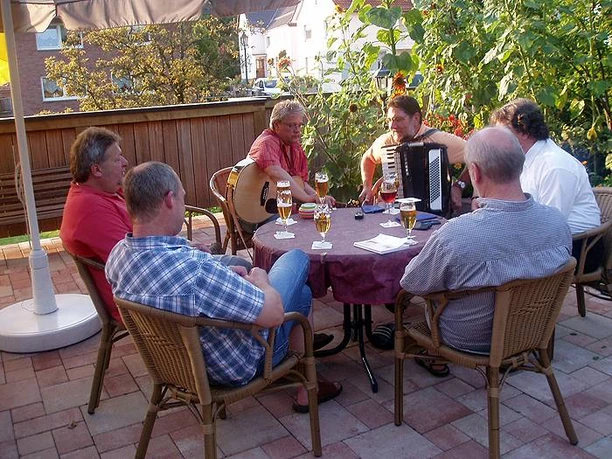 Aussengastronomie Gruppe von Männern sitzt bei Getränken draußen, mit Gitarre und Akkordeon für Musikunterhaltung.