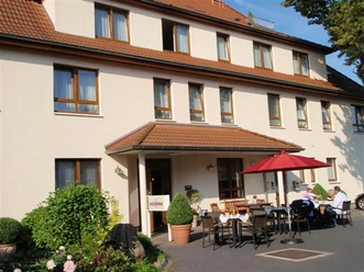 Frühstückstische draußen Hotel Hollmann Sonnige Terrasse mit gedeckten Tischen vor Hotel Hollmann, rote Schirme spenden Schatten.