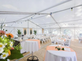 Großes Festzelt mit weißer Inneneinrichtung, Blumendekoration auf Tischen und Holzfußboden.