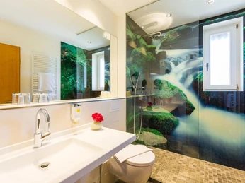 Bad im Germanenhof Sandebeck Modernes Badezimmer mit großflächigem Wasserfallmotiv an der Wand, Waschtisch und Dusche.