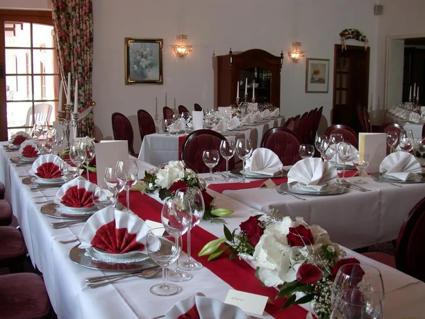 Festlich gedeckter Tisch mit weißen Tafeldecken, Rot-Weißen Blumenarrangements und eleganter Dekoration in einem Bankettsaal.