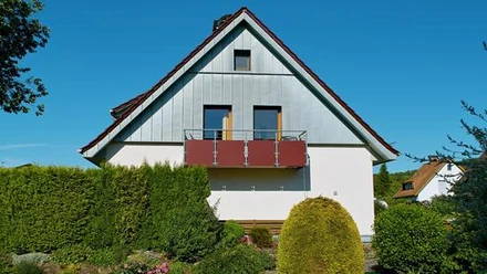 FeWo am SchiederSee Ferienwohnung mit moderner Fassade, Balkon und umgeben von grüner Gartenlandschaft unter blauem Himmel.