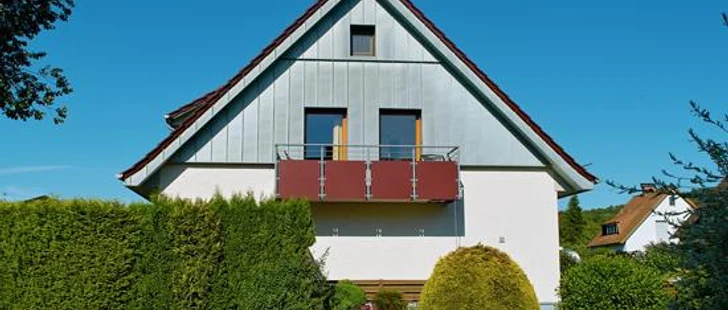 FeWo am SchiederSee Ferienwohnung mit moderner Fassade, Balkon und umgeben von grüner Gartenlandschaft unter blauem Himmel.