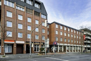 Außenansicht Backsteingebäude mit mehreren Stockwerken an einer Straße, rundum moderne Fensterfronten.