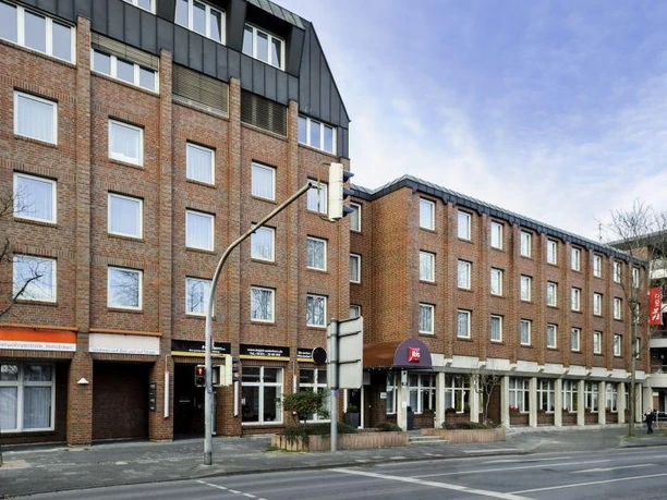 Außenansicht Backsteingebäude mit mehreren Stockwerken an einer Straße, rundum moderne Fensterfronten.