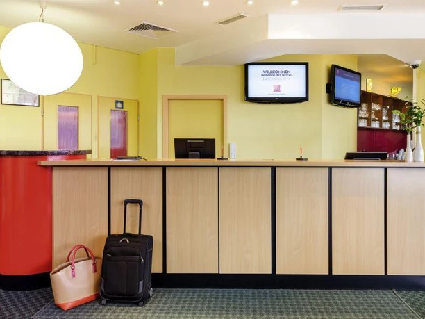 Empfang Empfangsbereich mit hellen Holztresen, links Koffer und Tasche, darüber eine große, leuchtende Lampe.