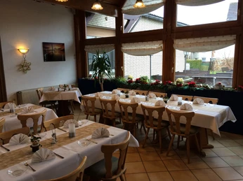 Gasthaus Engemann Gaststube mit Holzmöbeln, gedeckten Tischen, großen Fenstern und Pflanzen.