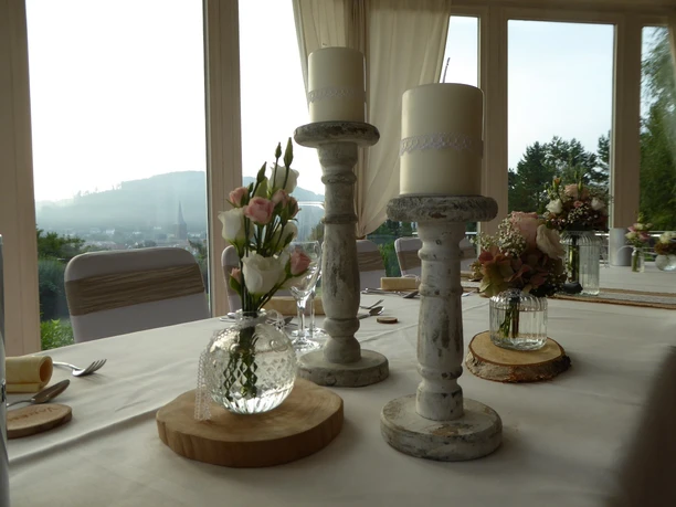 Ein stilvoll gedeckter Tisch in einem hellen Raum mit Kerzen, Blumen und Bergblick im Hintergrund.