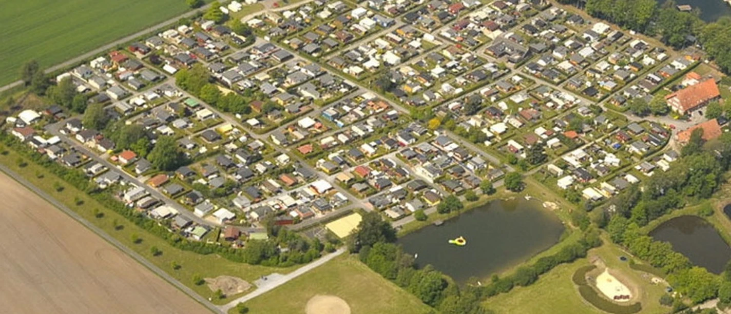 Luftaufnahme eines großen Campingplatzes mit Wohnmobilen, umgeben von Wald und zwei kleinen Seen.