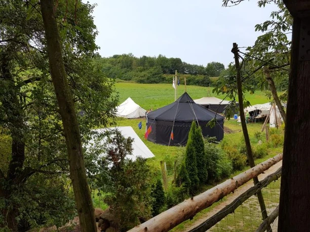 Zelte stehen auf einer grünen Wiese, umgeben von Bäumen und einem rustikalen Holzzaun.