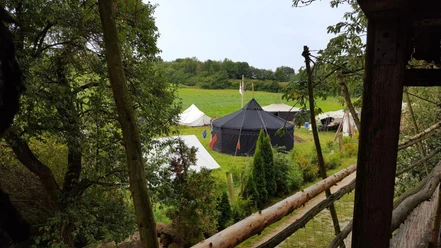 Zeltplatz Abenteuerland Warbug Zelte stehen auf einer grünen Wiese, umgeben von Bäumen und einem rustikalen Holzzaun.