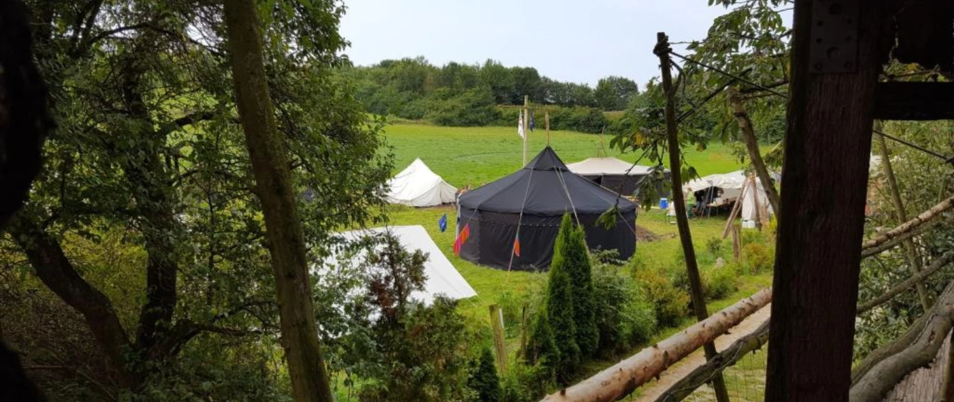 Zeltplatz Abenteuerland Warbug Zelte stehen auf einer grünen Wiese, umgeben von Bäumen und einem rustikalen Holzzaun.