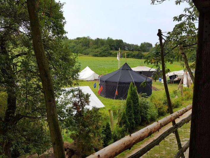 Zeltplatz Abenteuerland Warbug Zelte stehen auf einer grünen Wiese, umgeben von Bäumen und einem rustikalen Holzzaun.
