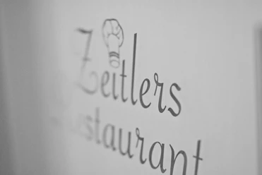 Schwarz-weiß-Fotografie des Schriftzugs "Zeitlers Restaurant" mit einem Kochmützen-Symbol.