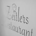 Schwarz-weiß-Fotografie des Schriftzugs "Zeitlers Restaurant" mit einem Kochmützen-Symbol.