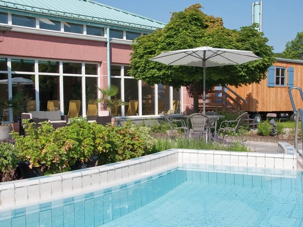 Außenbereich eines Schwimmbads mit glasklarem Wasser, Sonnenschirmen und gepflegtem Garten.