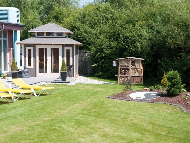 Grüner Außenbereich der Driburger Therme mit Liegestühlen, Gartenhaus und Insektenhotel.