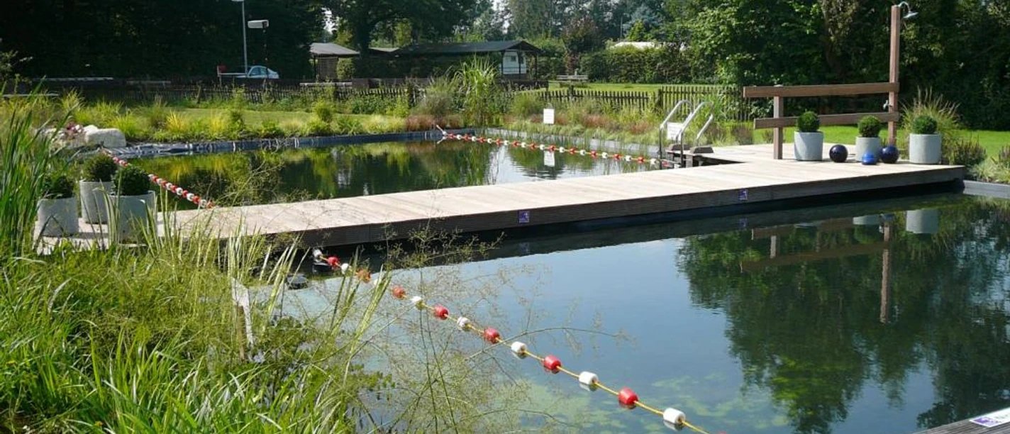 Rohloff Ferienpark Buschhof Extertal Schwimmteich mit Holzsteg, umgeben von üppiger Vegetation, im Rohloff Ferienpark Extertal.