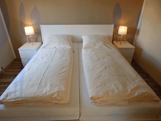 Ferienwohnung SchiederSee Hell eingerichtetes Doppelbett mit weißen Bettlaken, flankiert von zwei Nachttischen mit Lampen.