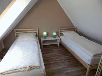 Zwei Einzelbetten in einem Dachzimmer mit schräge Wände, dazwischen ein kleiner Tisch mit Lampen.