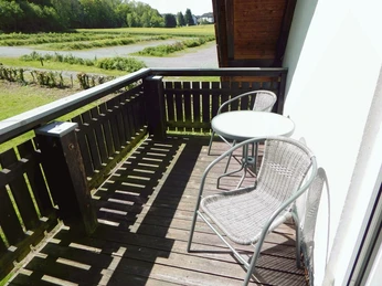 Ferienwohnung SchiederSee Zwei Rattan-Stühle und ein runder Tisch auf einem Holzbalkon mit Blick in eine grüne Landschaft.