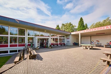 Aussenansicht Jugendherberge Bad Driburg Jugendherberge Bad Driburg mit Sonnenterrasse, Picknicktischen und großen Fenstern in modernem Design.