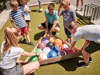 Spiel im Freien Juhendherberge Bad Driburg Kinder und Betreuer sammeln bunte Fußbälle auf einem grünen Kunstrasenplatz bei Sonnenschein.