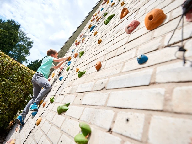 Ein Junge erklimmt eine Kletterwand mit bunten Griffen an der Jugendherberge Bad Driburg.